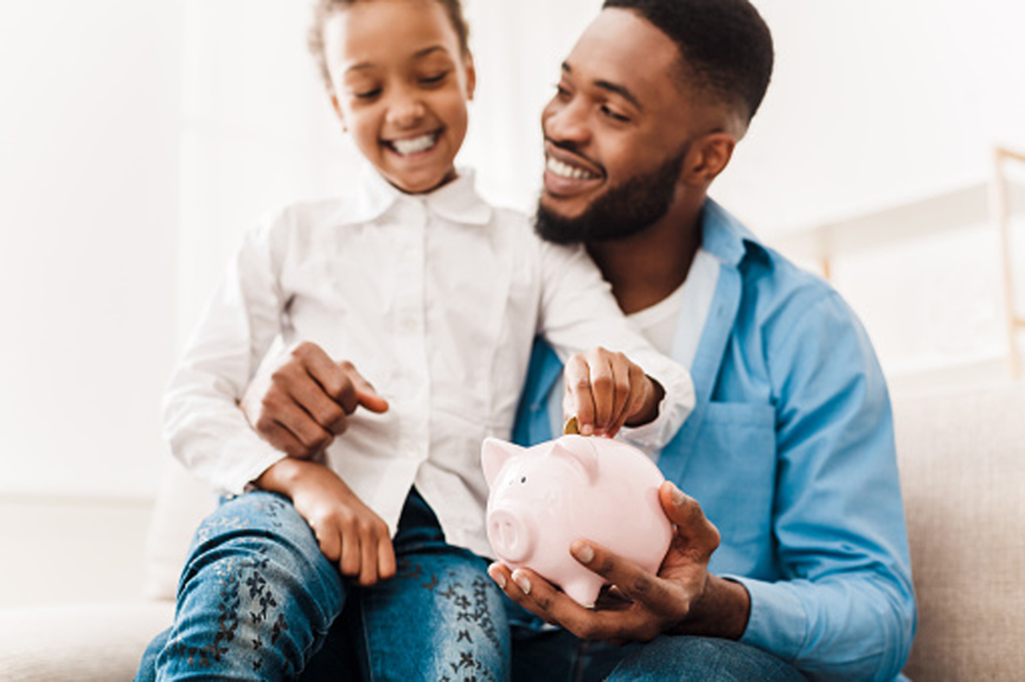 Man holding daughter while she puts money in a piggy bank