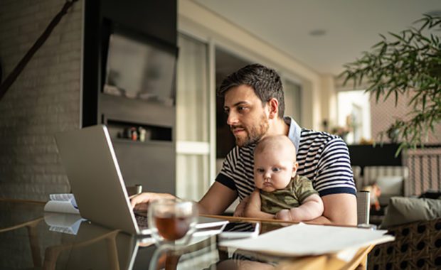 Man holding his son and working with laptop at home