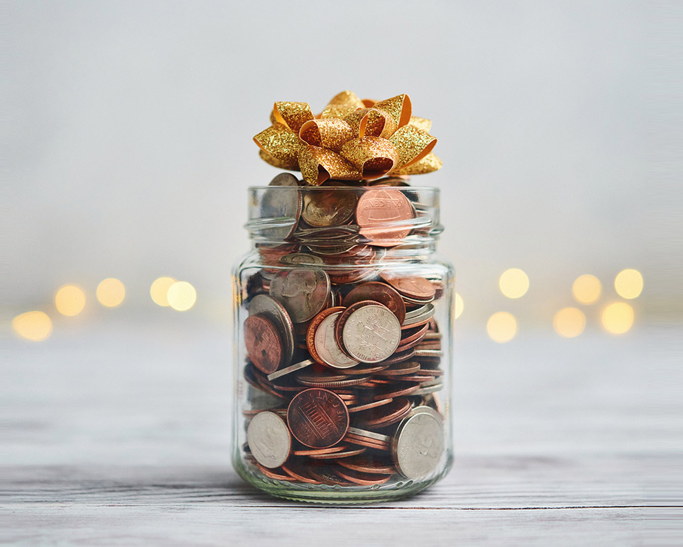 Jar filled with coins and bow in front of Christmas background with string lights